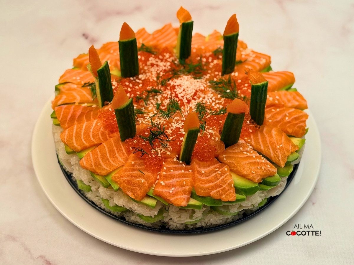 Gâteau de sushis présenté sur un plat avec des bougies comestibles réalisées avec des bâtonnets de concombre et du saumon fumé